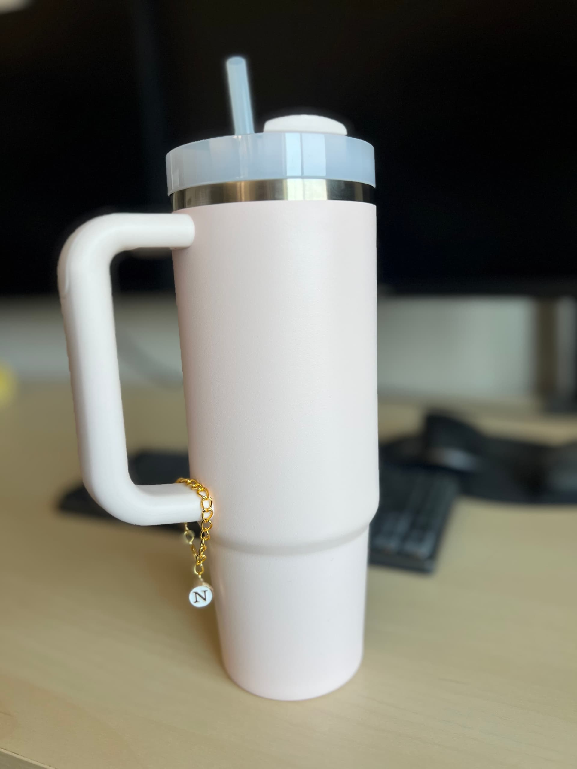 White initial charm clipped onto a pink Stanley tumbler